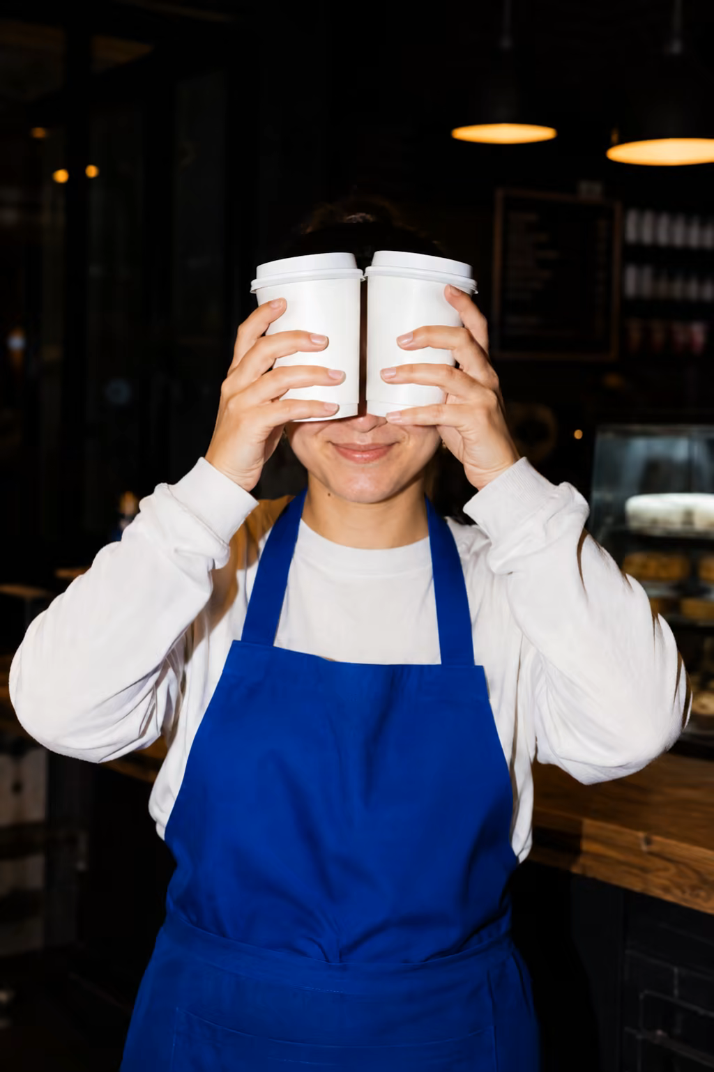 A café worker playfully holding two takeaway cups in front of their eyes